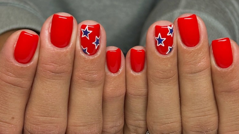 A person's hands with a red manicure an blue stars over two nails