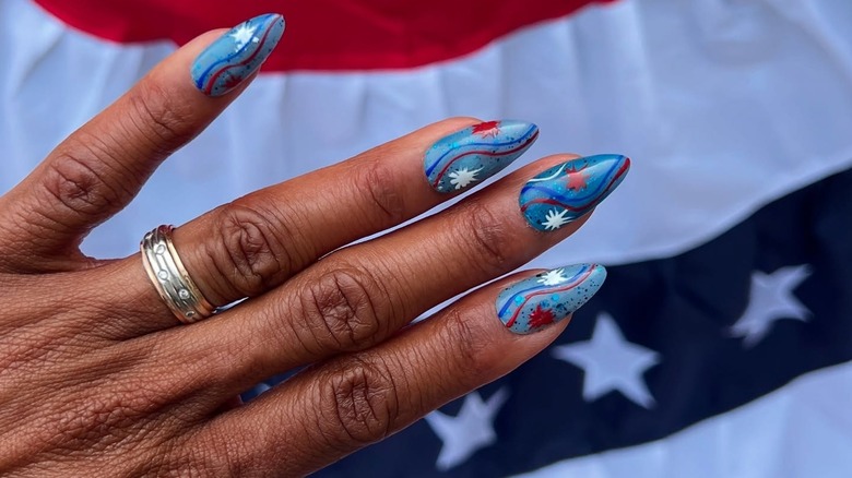 A woman's hand with a patriotic, red, white, and blue manicure in front of a flag