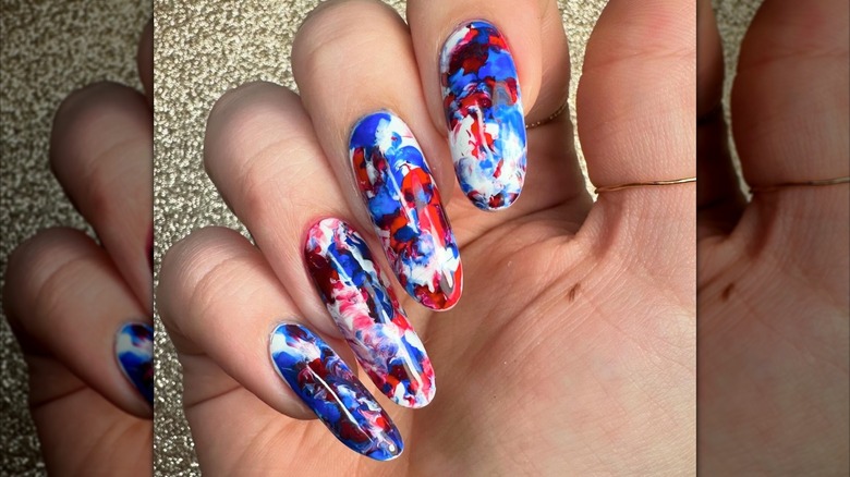 A person's hand with a red, white, and blue swirled manicure