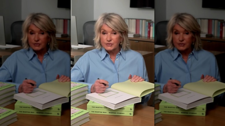 Martha Stewart sitting at a table and signing a stack of books