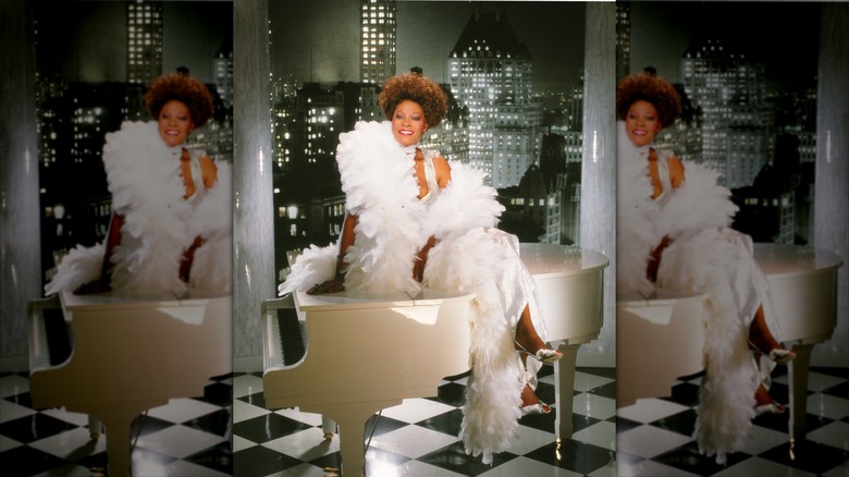 Dionne Warwick sits on a piano covered in white feathers