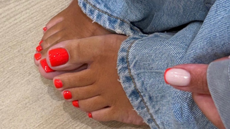 A person wearing blue denim jeans with a glossy, bright red pedicure