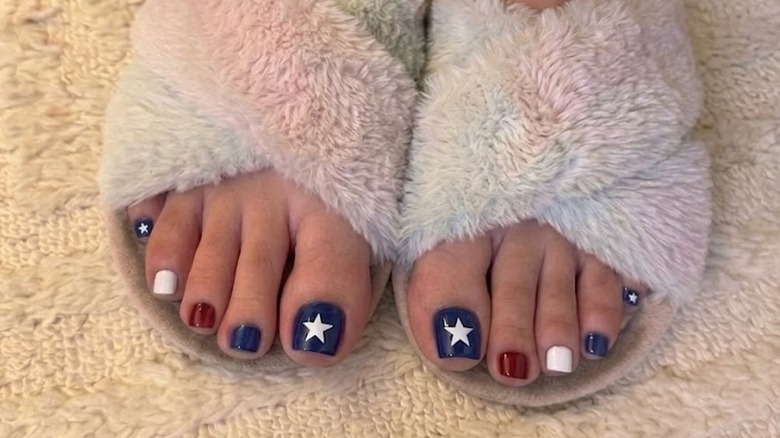 A person wearing fluffy slippers with an American flag inspired pedicure