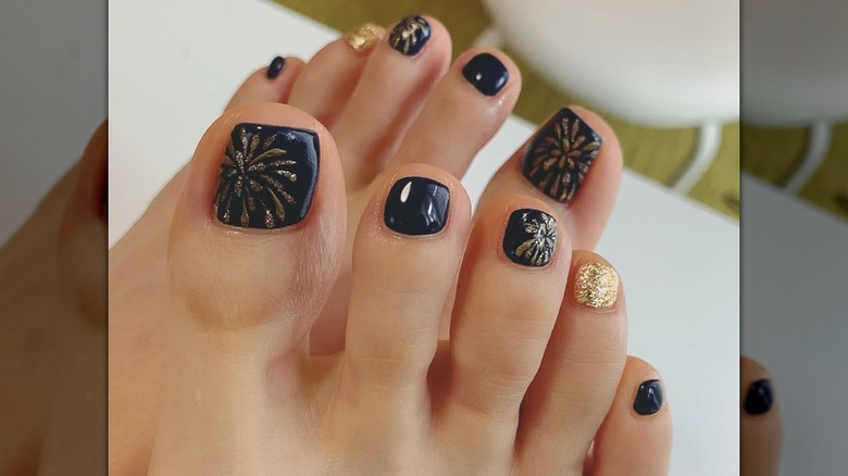 A dark navy pedicure with gold glitter designed to look like exploding fireworks