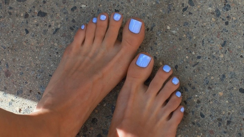 A woman standing on sand with a sky blue pedicure