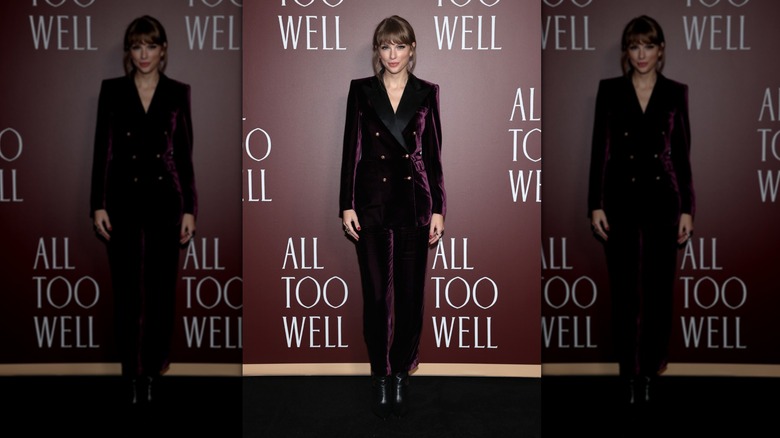 Taylor Swift poses wearing a burgundy velvet suit