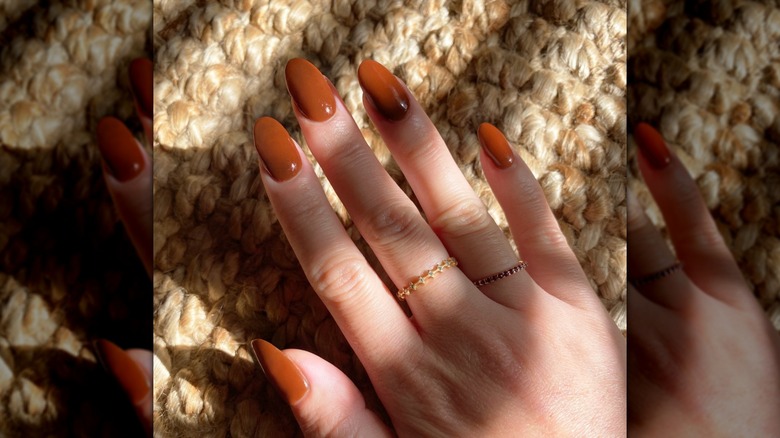 A woman showing her manicure with warm orange nail polish