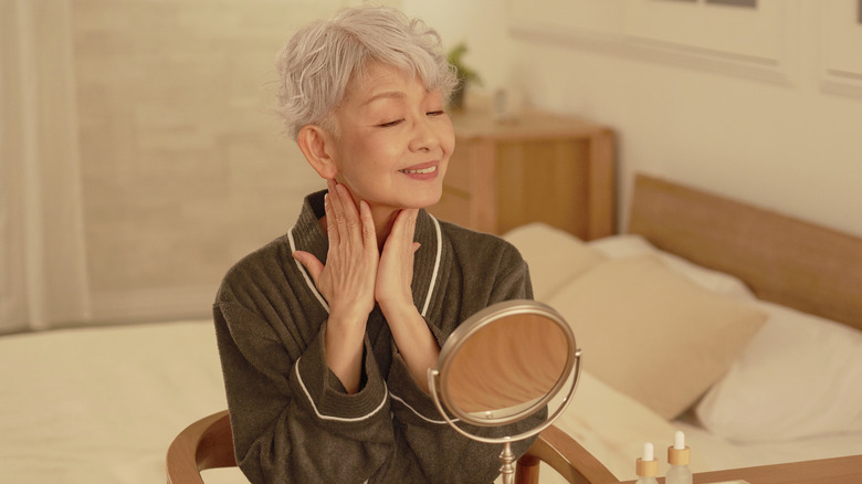 Older woman looking in mirror moisturizing skin