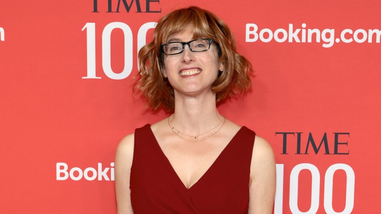 Freida McFadden smiling on the red carpet in front of a red background