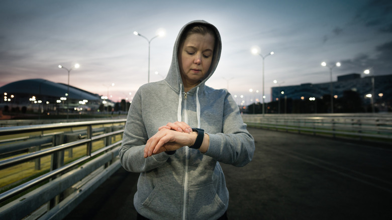 woman checks watch during evening jog