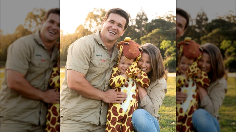 Bindi Irwin and Chandler Powell hugging their daughter Grace, a toddler who is dressed in a giraffe costume