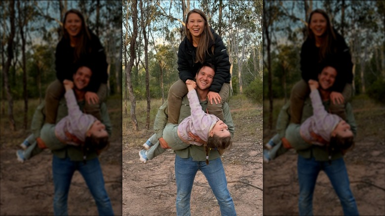 Bindi Irwin sitting on Chandler Powell's shoulders while he holds their daughter Grace