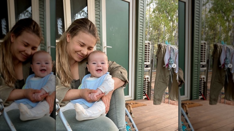 Bindi Irwin sitting on a porch and hugging her daughter Grace, a baby who is smiling