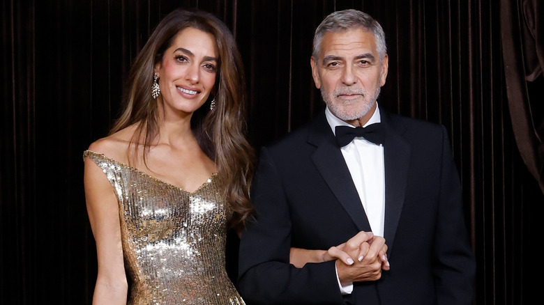 Amal Clooney holding hands with George Clooney at a fancy event, with her light-colored nails being visible
