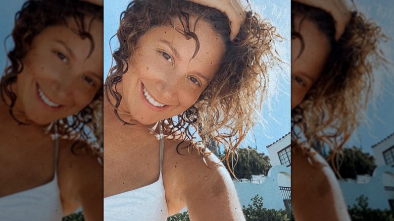 Ashley Tisdale smiling for a selfie while hold her curly hair out of her face