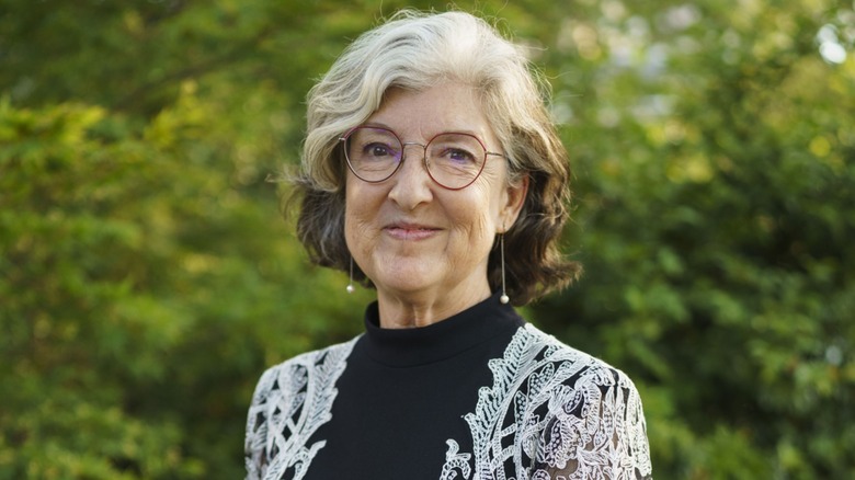 Barbara Kingsolver slightly smiling while standing in front of a foliage background