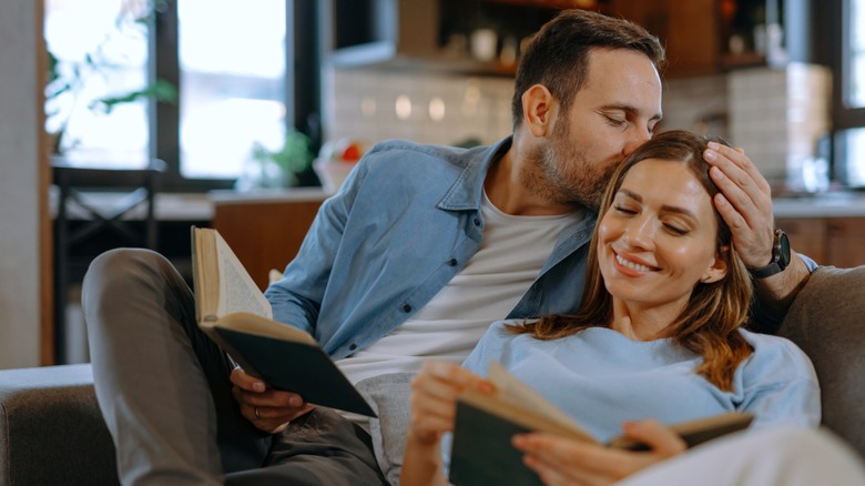 A man kissing a woman on the forehead as they both read books