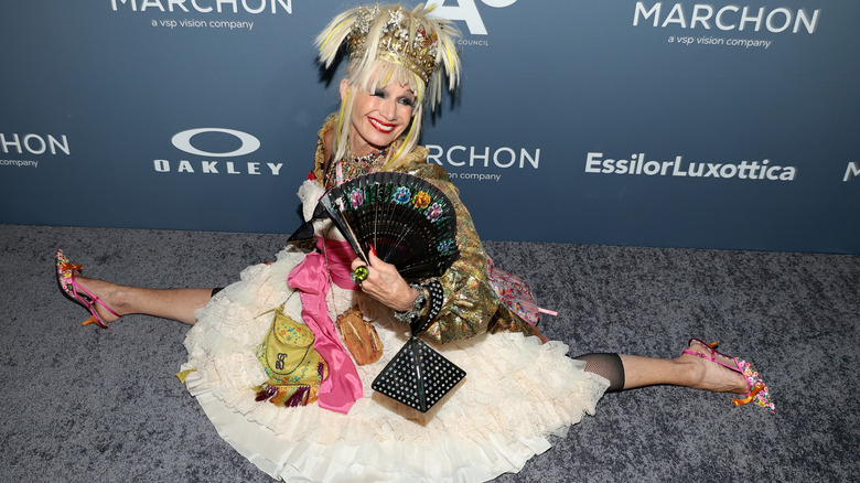 Betsey Johnson doing the splits on the red carpet in a tulle skirt with vibrant accessories