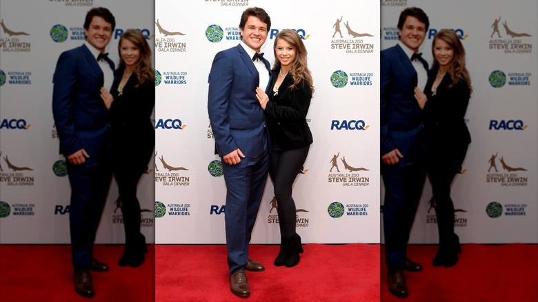 Bindi Irwin wearing an all-black outfit and posing on the red carpet with her husband