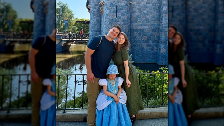 Bindi Irwin posing with her husband and daughter in front of the Disney castle
