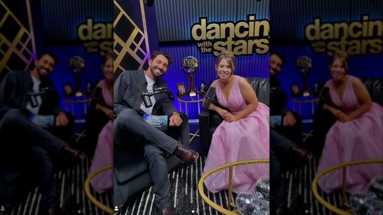 Bindi Irwin in a pink princess dress in a podcast studio and sitting next to a guy