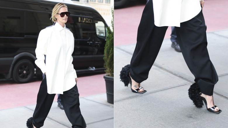 Charlize Theron walks wearing a white shirt and black trousers with feathered black heels