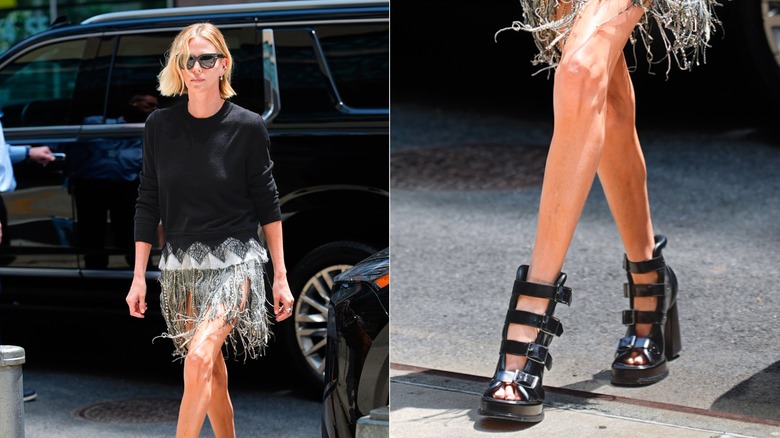 Charlize Theron walking wearing a fringe skirt, a black sweater, and chunky buckle sandals