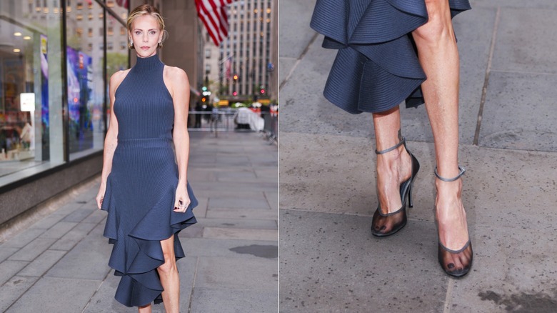 Charlize Theron poses wearing a turtleneck navy dress with a ruffled skirt and sheer black heels