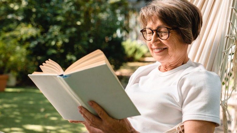 Elderly woman relaxing while reading a book in a hammock outdoors