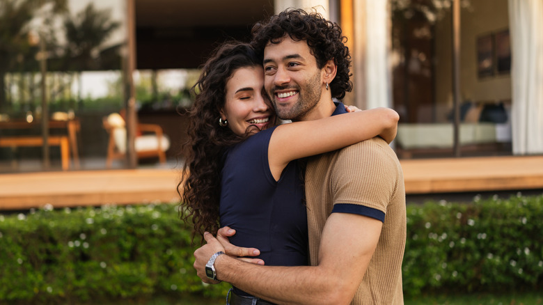 A couple hug outside a house