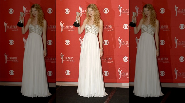 Taylor Swift on the red carpet in a white gown and holding an award