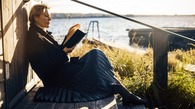 A woman sitting by the water reading a book
