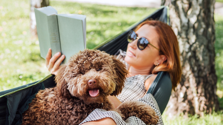 A woman in a hammock with her dog reading a book outside