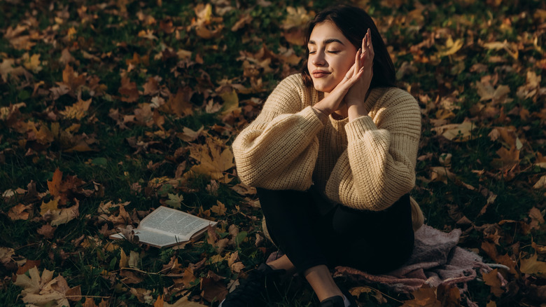 Young woman enjoying autumn outdoors with book beside her