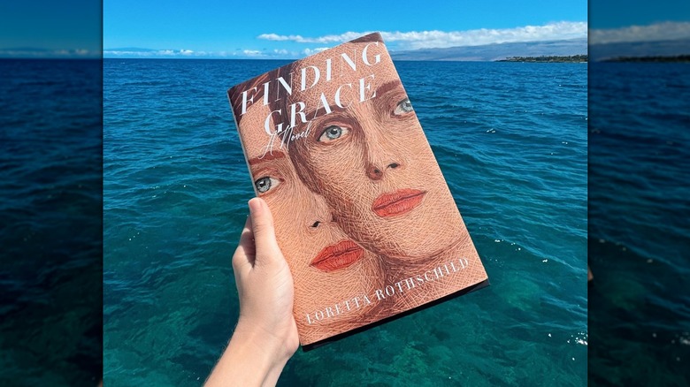 A person holding a copy of Finding Grace by Loretta Rothschild over water