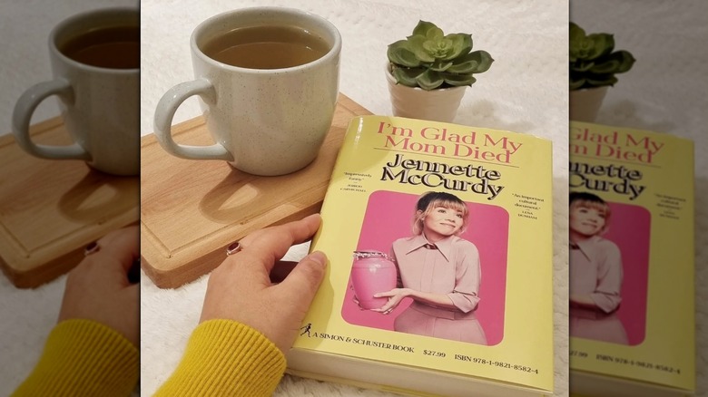 A copy of "I'm Glad My Mom Died" on a table next to a cup of tea