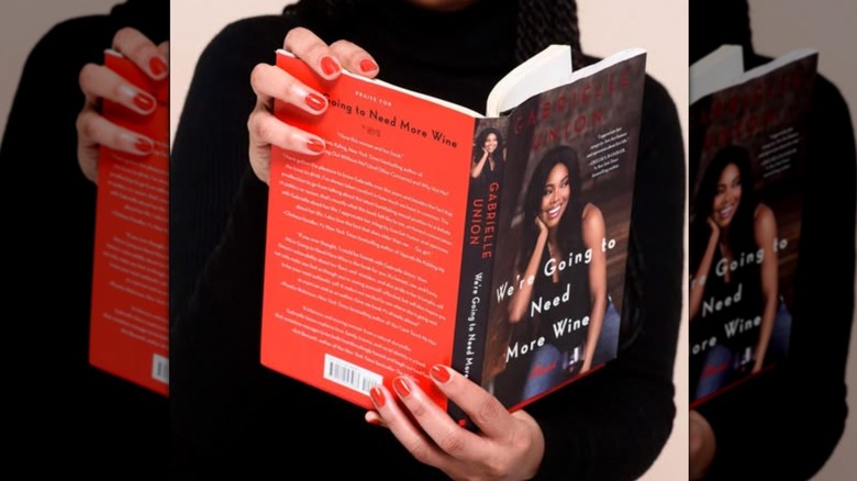 Hands holding a copy of "We're Going to Need More Wine" open to read