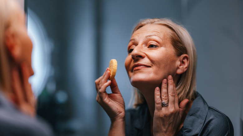 An older woman applying foundation with a sponge