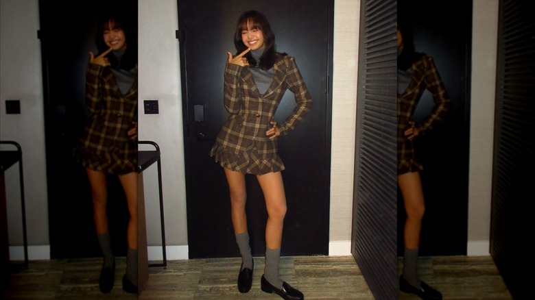 Lisa posing in front of a black door, wearing a matching plaid skirt and blazer
