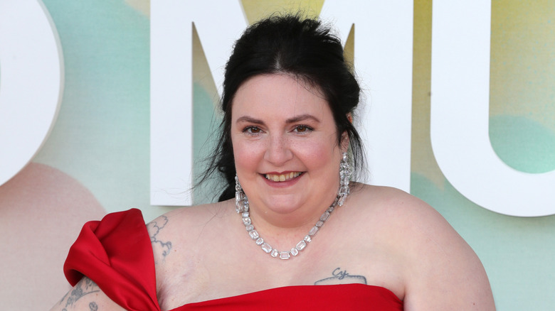 Close-up picture of Lena Dunham smiling on the red carpet, in a red dress
