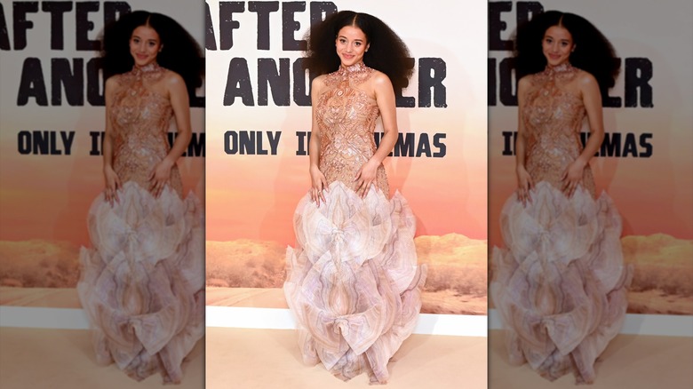 Chase Infiniti attending the London premiere of "One Battle After Another" in a bronze-colored gown with dramatic, exaggerated skirt