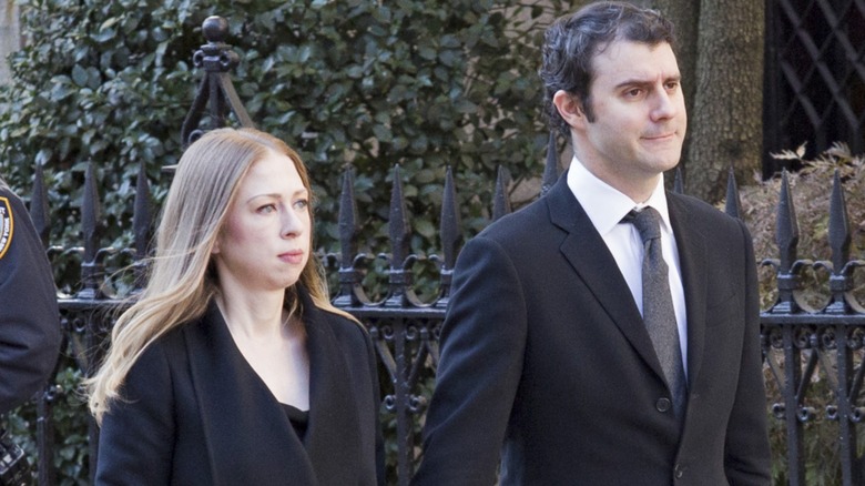 Chelsea Clinton and Marc Mezvinsky walking outside hand in hand wearing all black