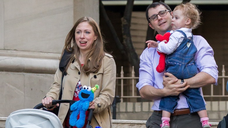 Chelsea Clinton pushing a stroller on the street while walking alongside Marc Mezvinsky holding one of their children