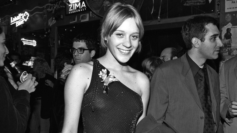 Black-and-white photo of Chloë Sevigny smiling at an afterparty while wearing a sparkly, one-shouldered dress