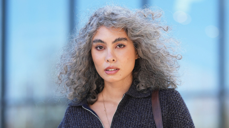 A woman with curly gray hair wearing a charcoal toned sweater.