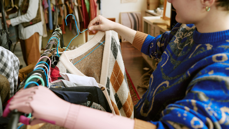 Person shopping for sweaters at thrift store