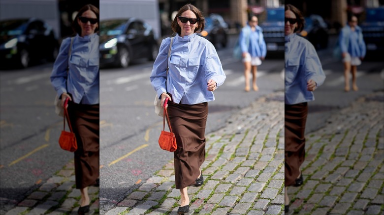 A woman walking the streets in a blue shirt with a brown skirt