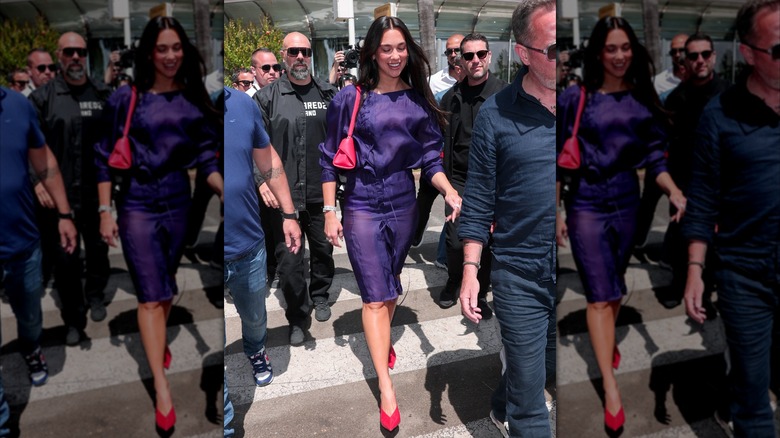 Dua Lipa walking in a crowd in a purple dress with a red bag and shoes