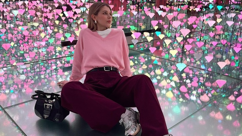 A woman sitting amongst strings of multi-colored diamond lights in a pink sweater with burgundy pants