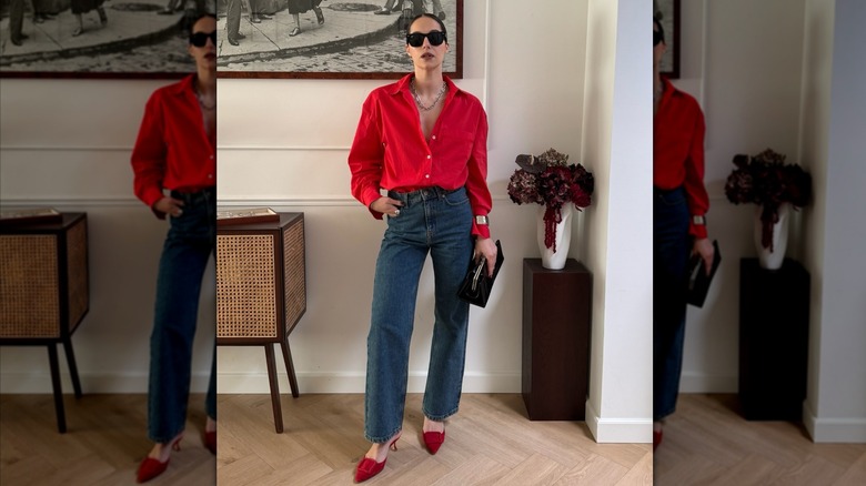 A woman posing while wearing a red shirt with blue jeans and red shoes